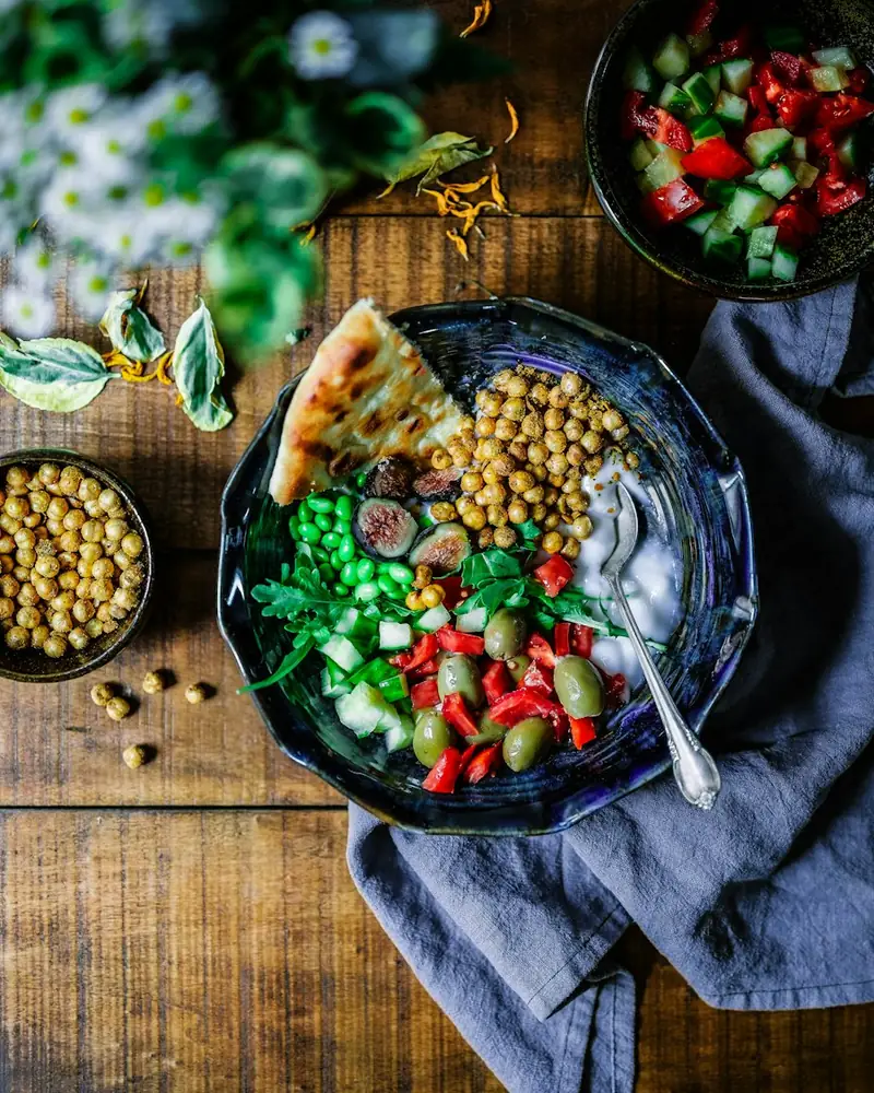 A bowl of chickpeas, greens and fresh vegetables on a wooden table